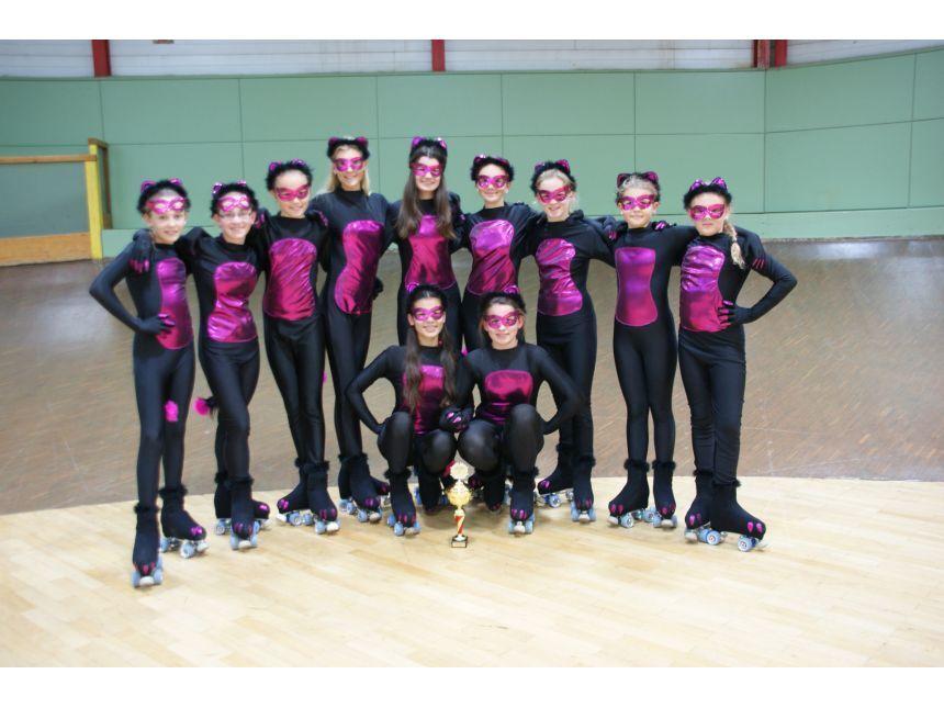 Gruppe von neun jungen Rollschuhl&auml;uferinnen in Catwoman-Kost&uuml;men mit einer Troph&auml;e auf einer Holzfl&auml;che.