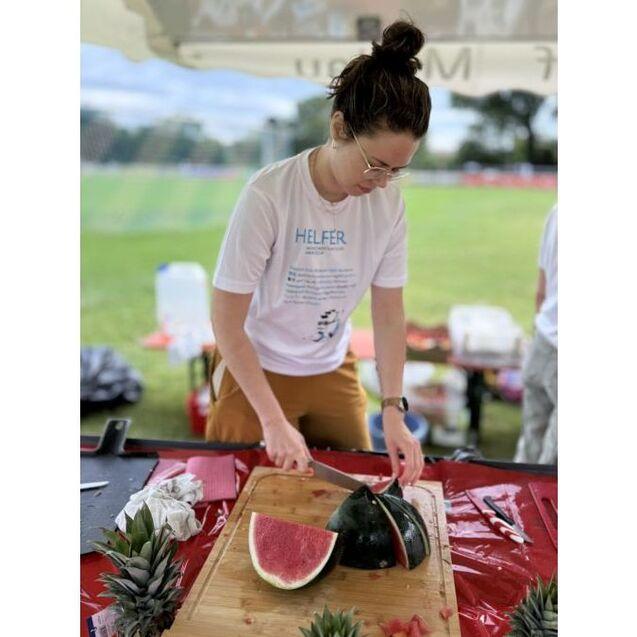 Frau schneidet eine Wassermelone auf einem Holzbrett, umgeben von Ananasst&uuml;cken auf einem festlichen Tisch.