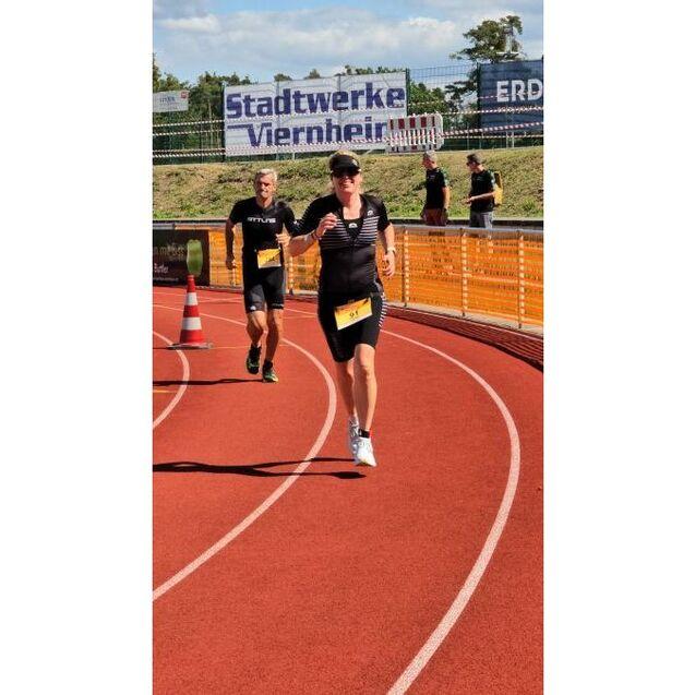 Zwei L&auml;ufer in Sportkleidung sprinten auf einer roten Laufbahn bei einem Wettkampf, umgeben von Zuschauern.