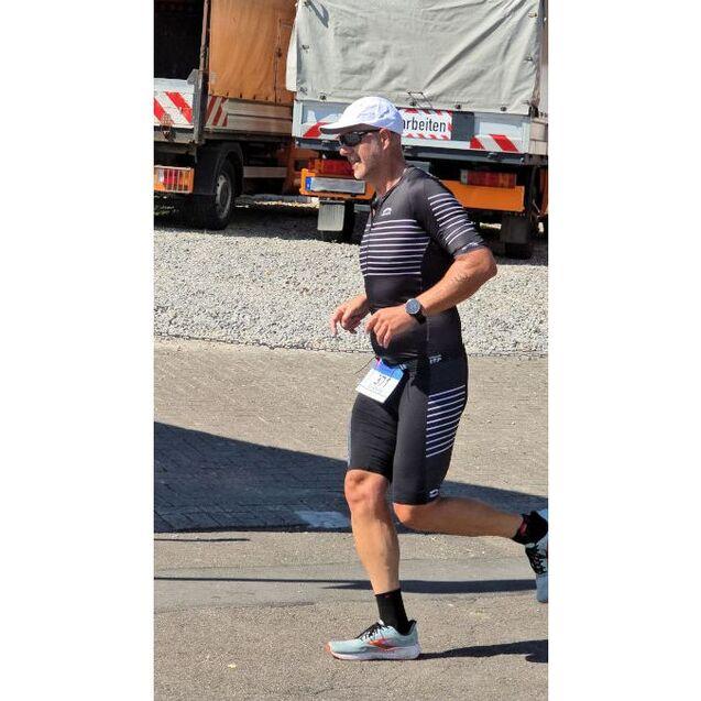 Ein athletischer Mann in Sportkleidung l&auml;uft bei einem Wettkampf auf einer befestigten Strecke.