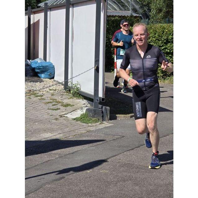L&auml;ufer in Sportmontage sprintet auf Asphaltweg, im Hintergrund ein weiterer Jogger gibt Daumen hoch.