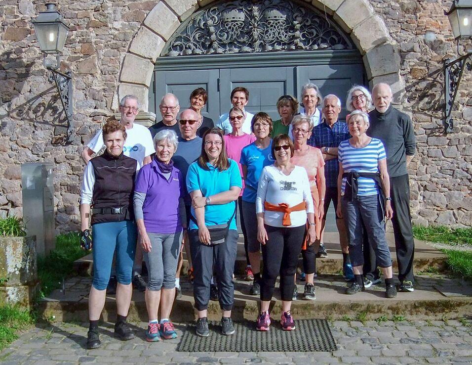Gruppe von 20 Personen verschiedener Altersgruppen vor einem historischen Geb&auml;ude, umgeben von Steinmauern und Laternen.