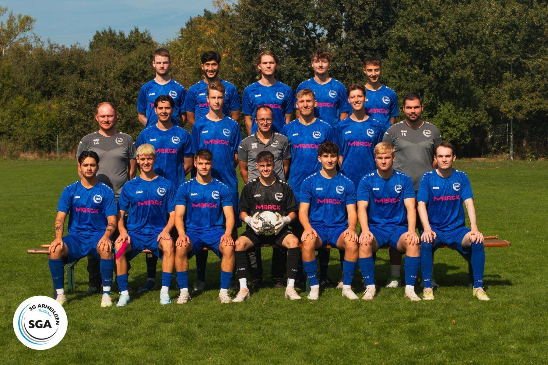 Mannschaftsbild von Fußballspielern in blauen Trikots, stehend und sitzend auf einer grünen Wiese.