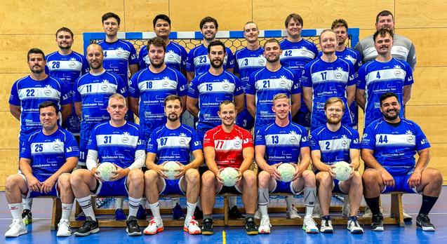 Gruppenfoto von 20 Handballspielern in blauen Trikots, posierend in einer Sporthalle mit B&auml;llen in der Hand.