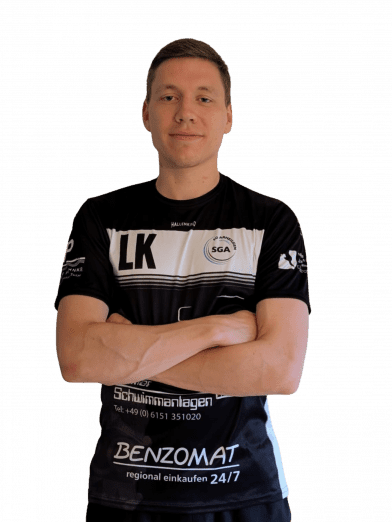 Portr&auml;t eines Mannes mit verschr&auml;nkten Armen in einem schwarz-wei&szlig;en Sporttrikot mit Sponsorenlogos.