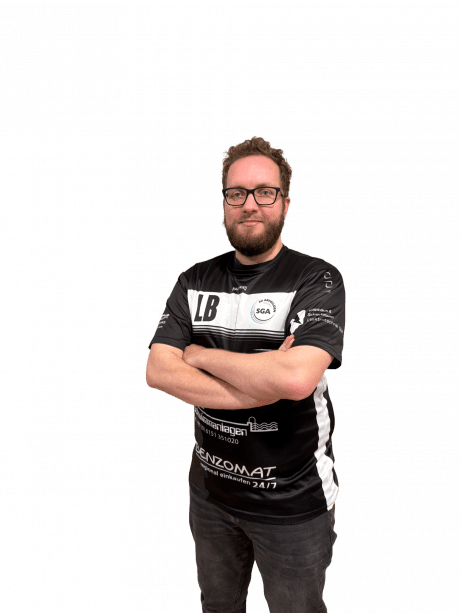 Mann mit Brille im schwarzen Sporttrikot steht mit verschr&auml;nkten Armen vor schwarzem Hintergrund.