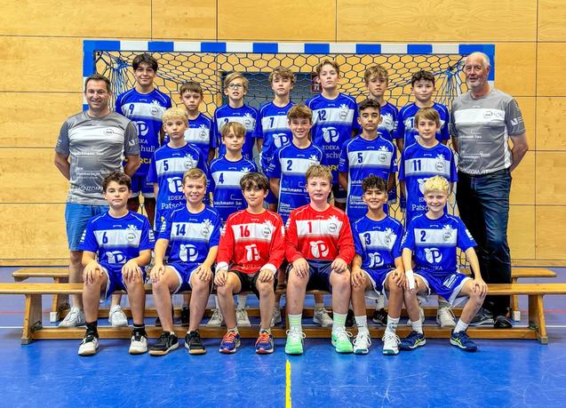 Gruppenbild einer Handballmannschaft aus Kindern in blauen und roten Trikots, posierend vor einem Tor.