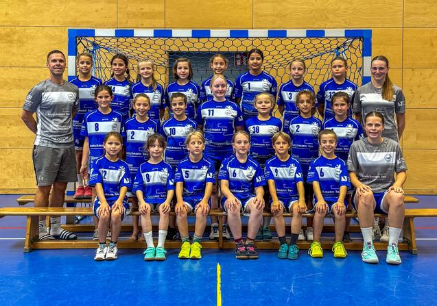 Gruppenfoto eines Handballteams mit 20 M&auml;dchen in blauen Trikots und zwei Trainerinnen vor einem Tor.