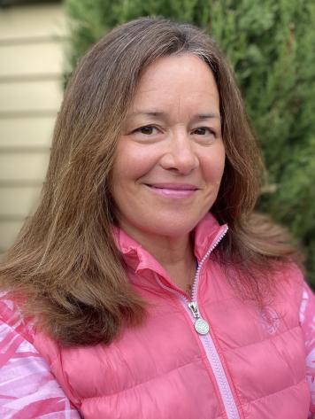 Nahaufnahme einer Frau mit langen, glatten Haaren, die eine rosa Weste tr&auml;gt, vor einem gr&uuml;nen Hintergrund.
