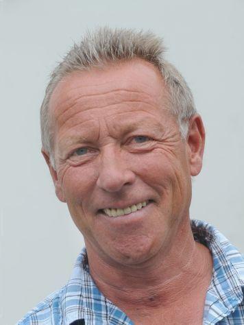 Portr&auml;t eines l&auml;chelnden Mannes mit blonden Haaren und fliederfarbenem Hemd auf neutralem Hintergrund.