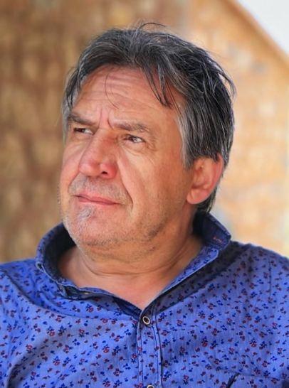 Portr&auml;t eines Mannes mit grauen Haaren, der nachdenklich schaut, in einem bordeauxfarbenen Hemd mit blauen Mustern.