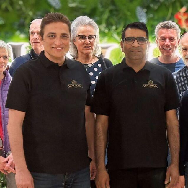 Gruppe von Personen steht lächelnd zusammen, alle tragen schwarze Poloshirts mit dem Logo „Shalimar“.
