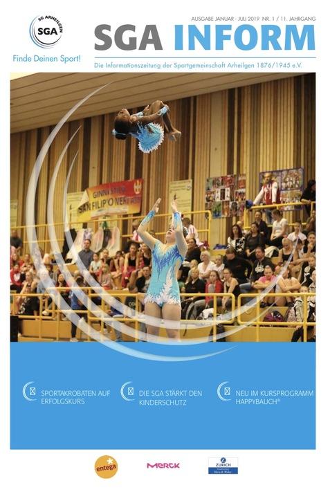 Zwei Sportlerinnen führen eine akrobatische Darbietung in einer Sporthalle vor Publikum auf.