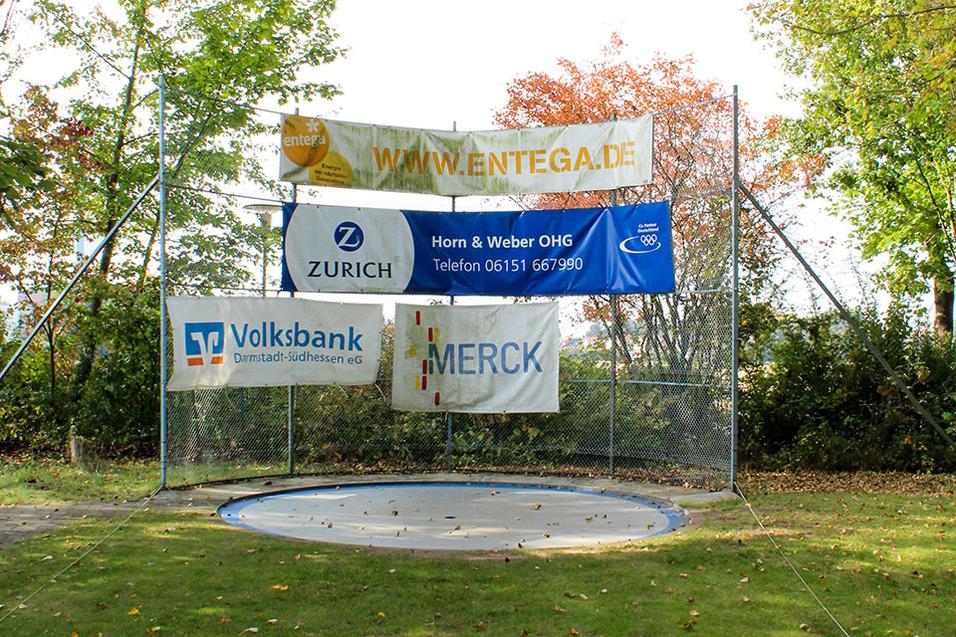 Platz mit einem Trampolin und mehreren Werbebannern, eingerahmt von B&auml;umen im Hintergrund.