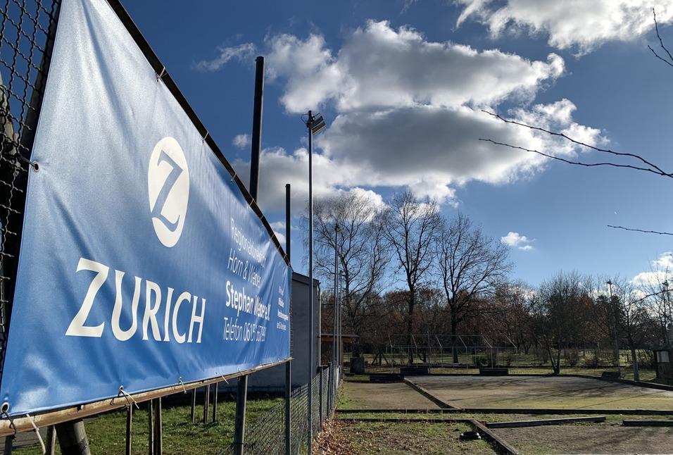 Banner der Zurich Versicherung an einem Sportplatz, im Hintergrund B&auml;ume und blauer Himmel mit Wolken.