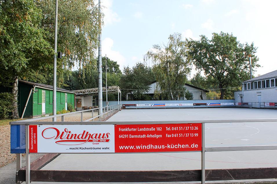 Offene Sportfläche mit einer Werbetafel von Windhaus, umgeben von Bäumen und Gebäuden in Darmstadt-Arheilgen.