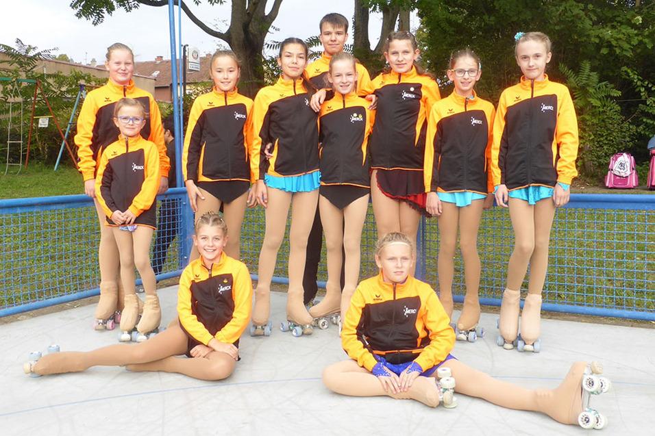 Gruppe von zehn Rollschuhläufern in einheitlicher Sportkleidung aus schwarzem und orangefarbenem Material auf einer Fläche.