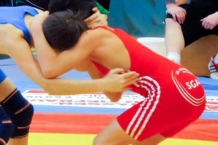 Zwei Ringer in roten und blauen Anz&uuml;gen im Wettkampf, stehen im mattenring und greifen sich aneinander.