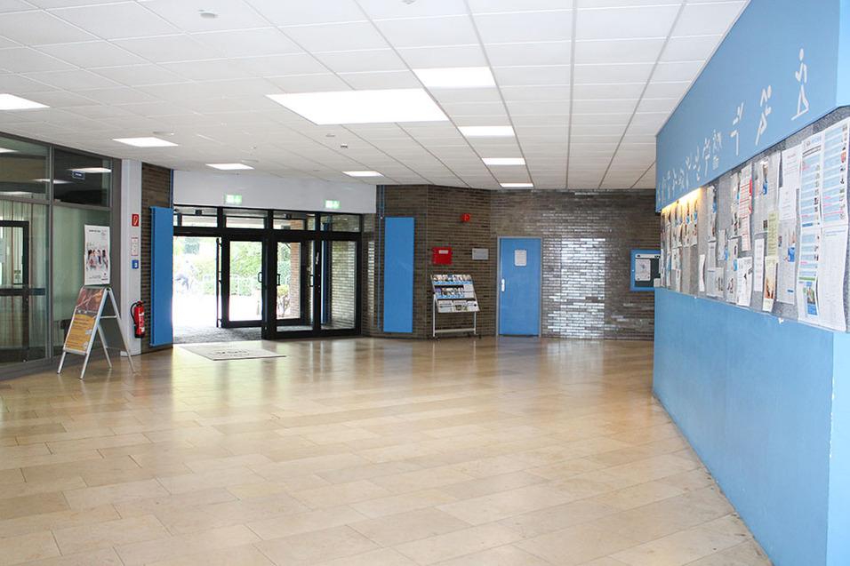 Heller Eingangsbereich mit Türen, Informationsständen und blauer Wand, an der zahlreiche Aushänge befestigt sind.