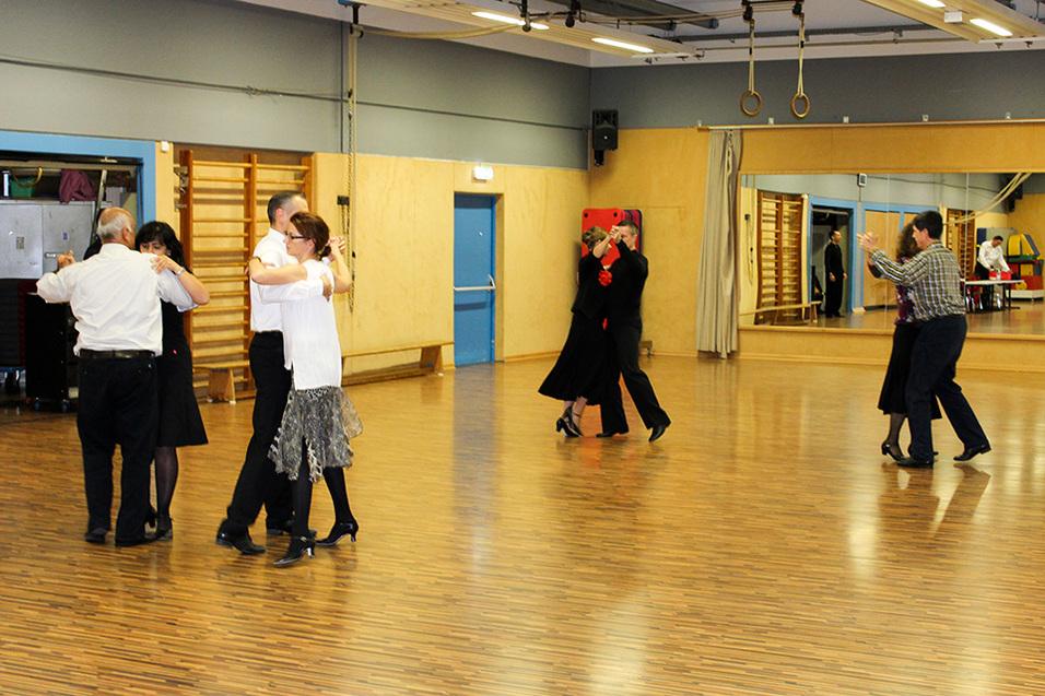 Tanzende Paare in einem Raum mit Holzfu&szlig;boden und Spiegeln, w&auml;hrend sie elegant miteinander kommunizieren.