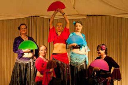 F&uuml;nf Frauen in folkloristischen Kost&uuml;men tanzen mit bunten F&auml;chern auf einer B&uuml;hne.