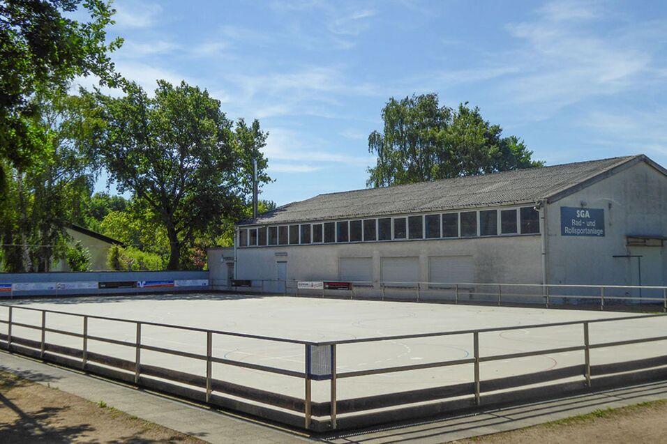 Rollschuhplatz mit einem Gebäude im Hintergrund, umgeben von Bäumen und klarem Himmel.
