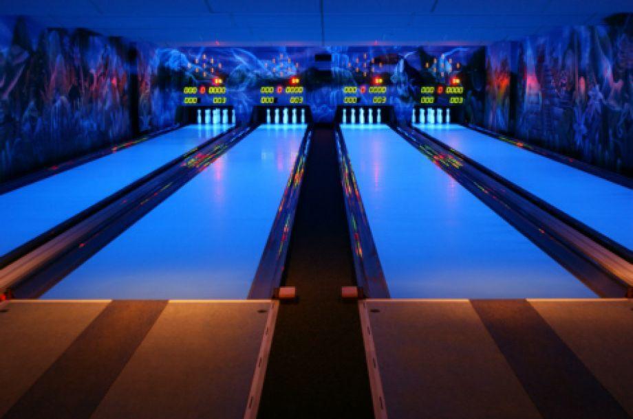 Bowlingbahn mit leuchtenden Bahnen und Pins im Hintergrund, umgeben von farbenfrohem Wanddesign.