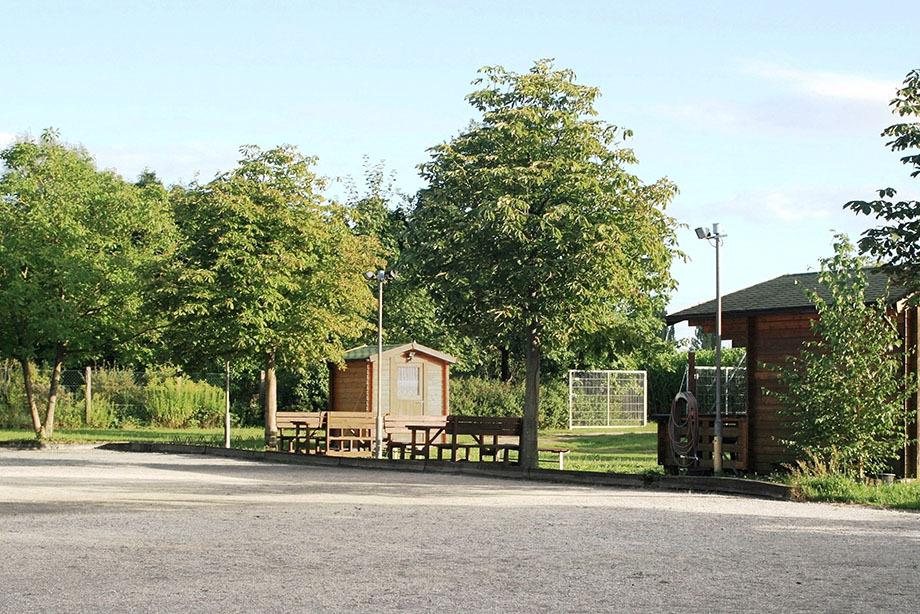 Landschaft mit Holzunterständen und Bänken umgeben von Bäumen auf einem gepflegten Gelände.